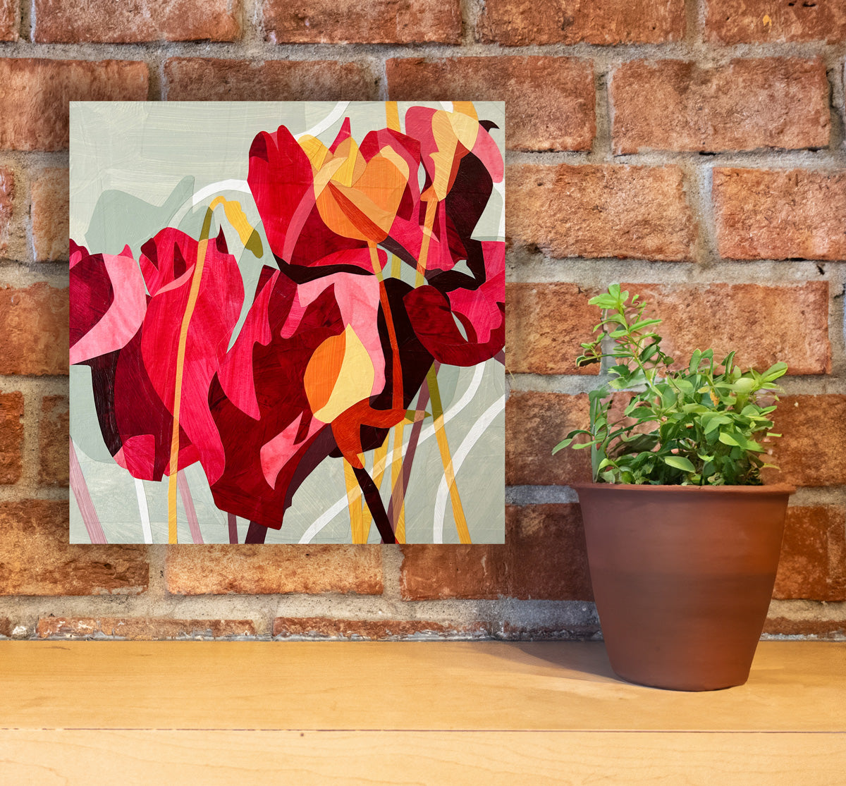 A colorful abstract floral artwork on a wall, featuring predominantly red and pink tones with touches of yellow and green hanging on a brick wall.