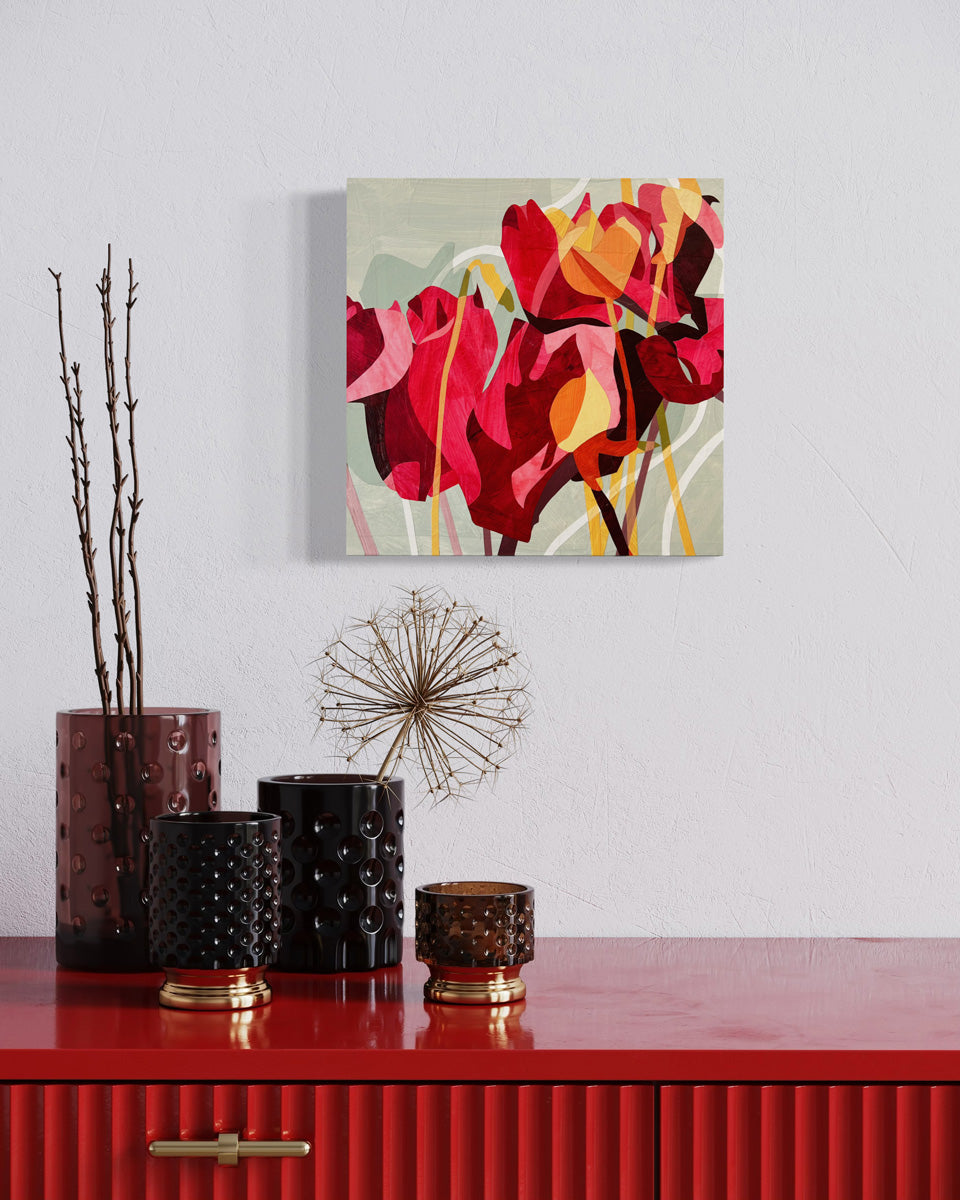 A colorful abstract floral artwork on a wall, featuring predominantly red and pink tones with touches of yellow and green hanging on a white wall over a red lacquered chest.