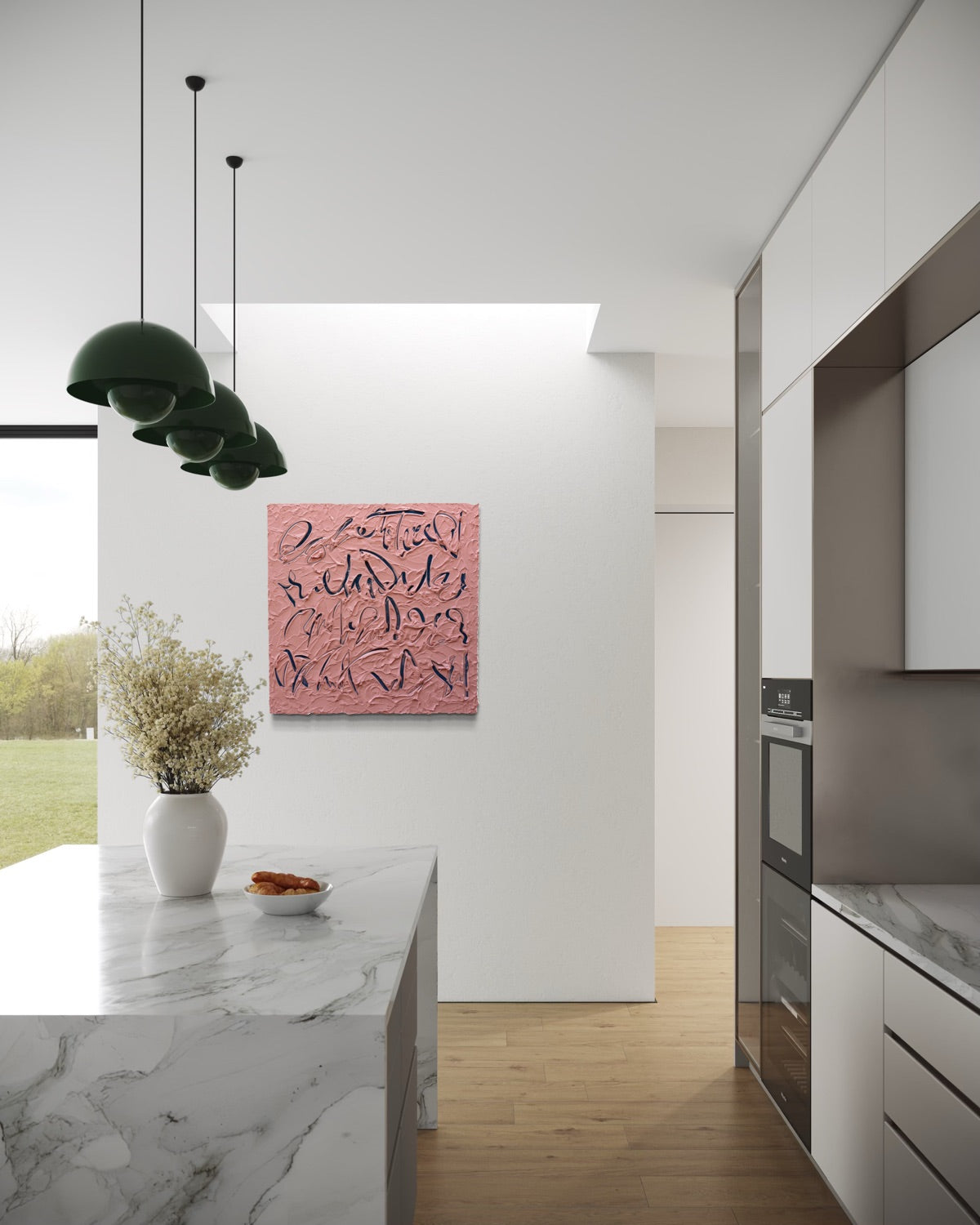 A coral pink text based painting with navy abstract calligraphic lines hangs on a white wall in a modern kitchen with white cabinets, a marble island, and green pendant lights.