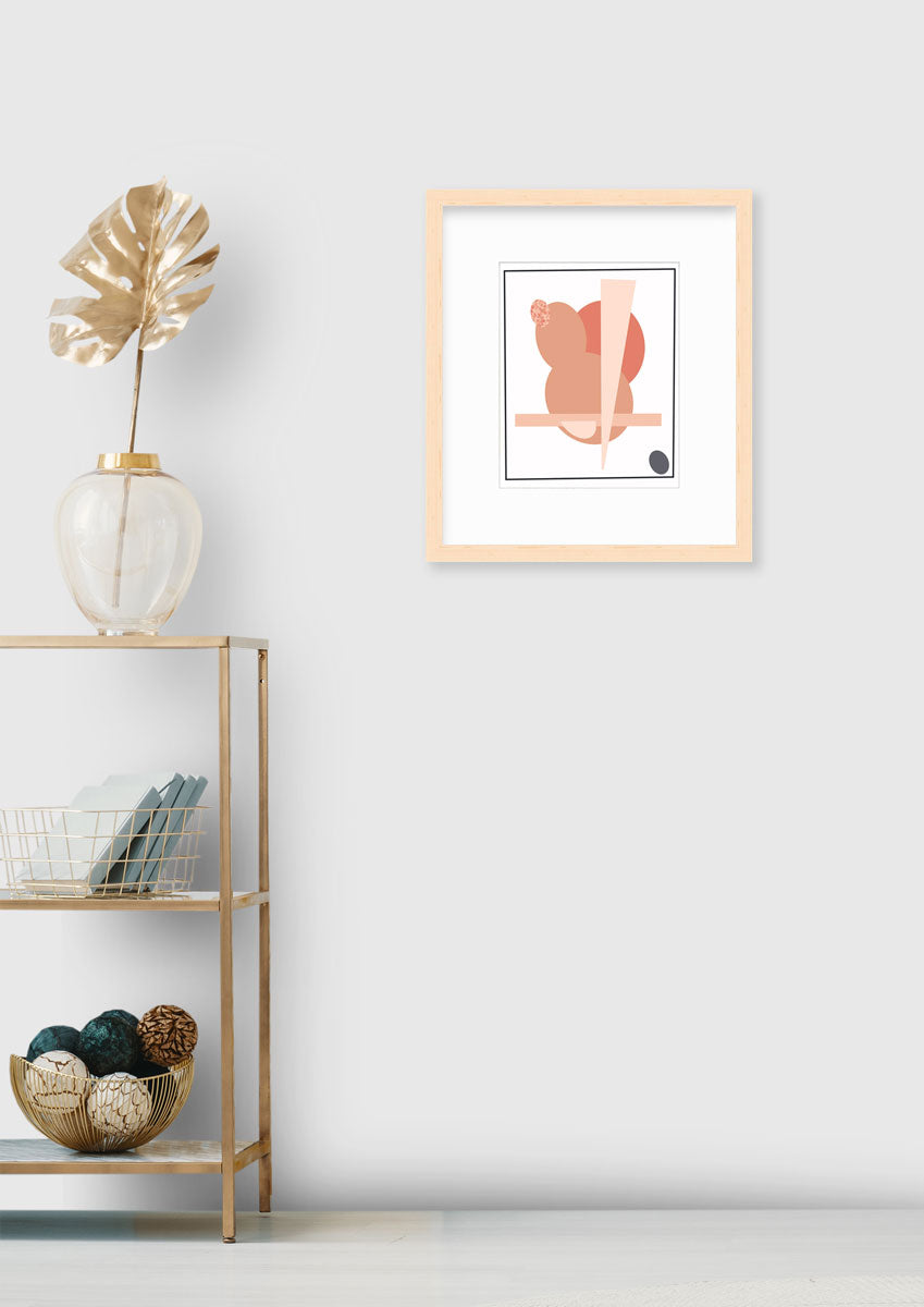 An abstract pink and grey art print in a neutral wood frame hangs on a light wall next to a gold console table with metallic table decor.