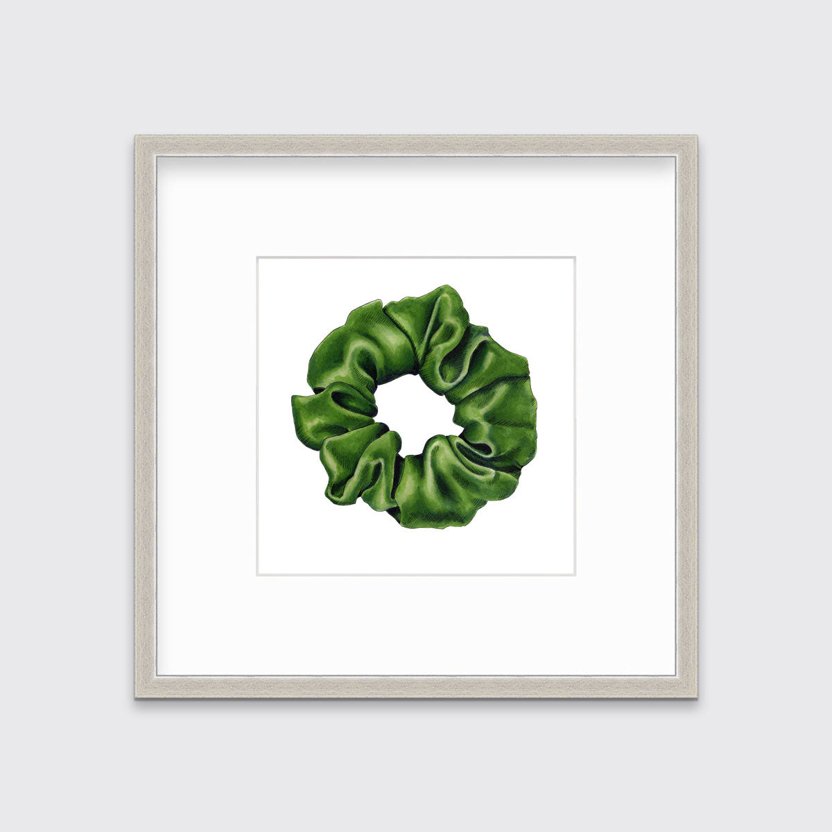 A drawing of a green hair scrunchie framed in a silver frame hangs on a white wall.
