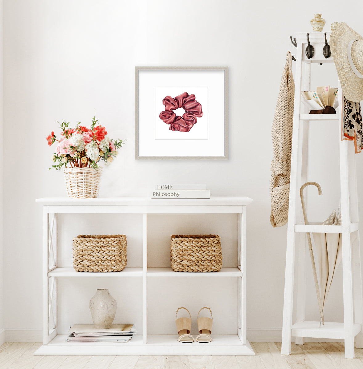 A drawing of a pink hair scrunchie framed in a silver frame hangs on a light wall above a white shelving unit with wicker decor and women's shoes, and next to a coat rack with women's accessories.