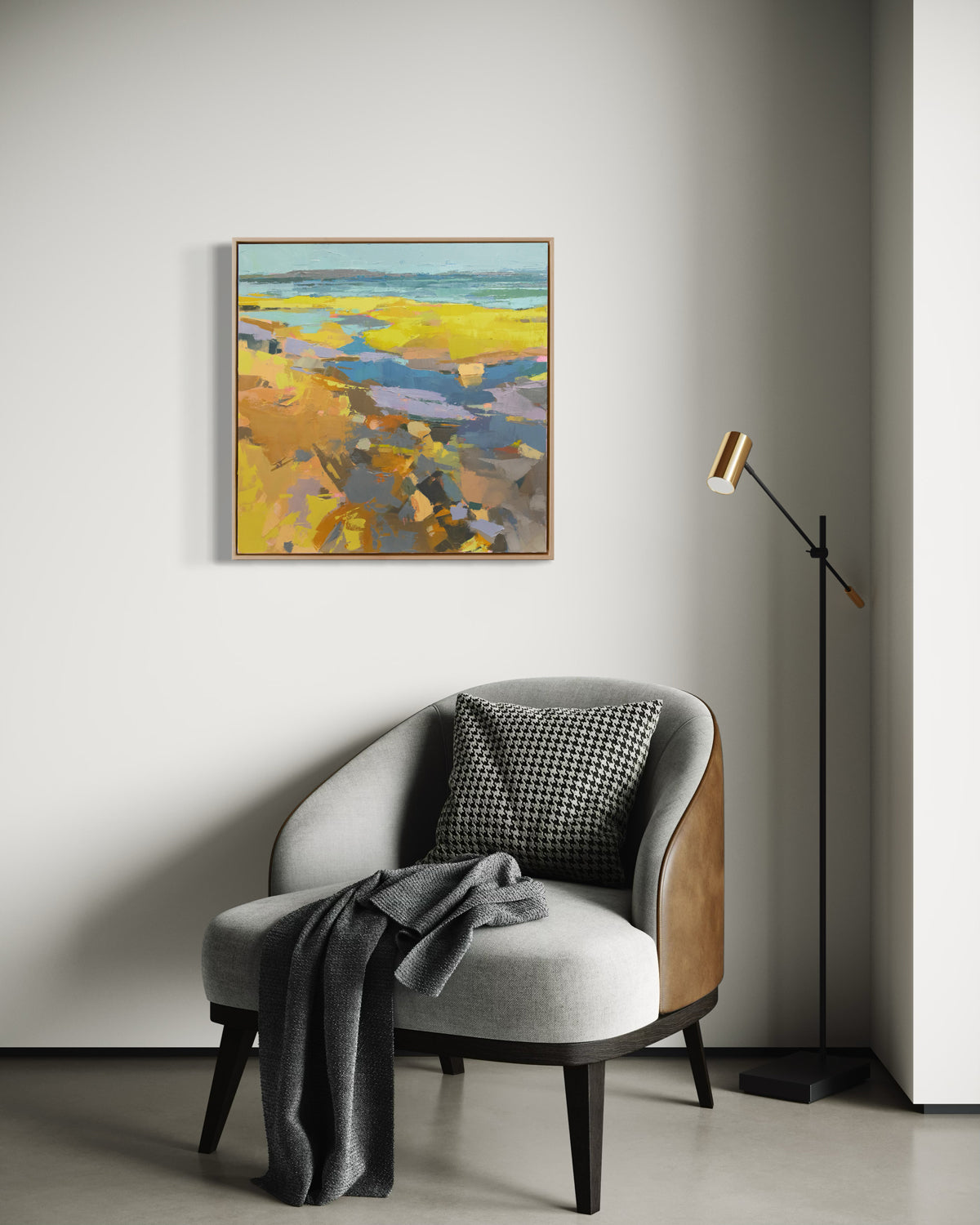 A blue and yellow abstract landscape painting hangs on a white wall over a grey chair with a grey throw and a pillow.