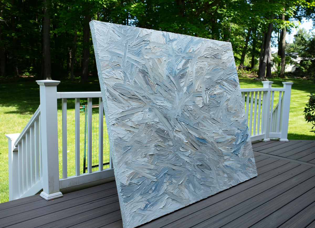 Original abstract painting by Teo Guererra with blue and gray tones on a wooden deck at her studio. Side view.