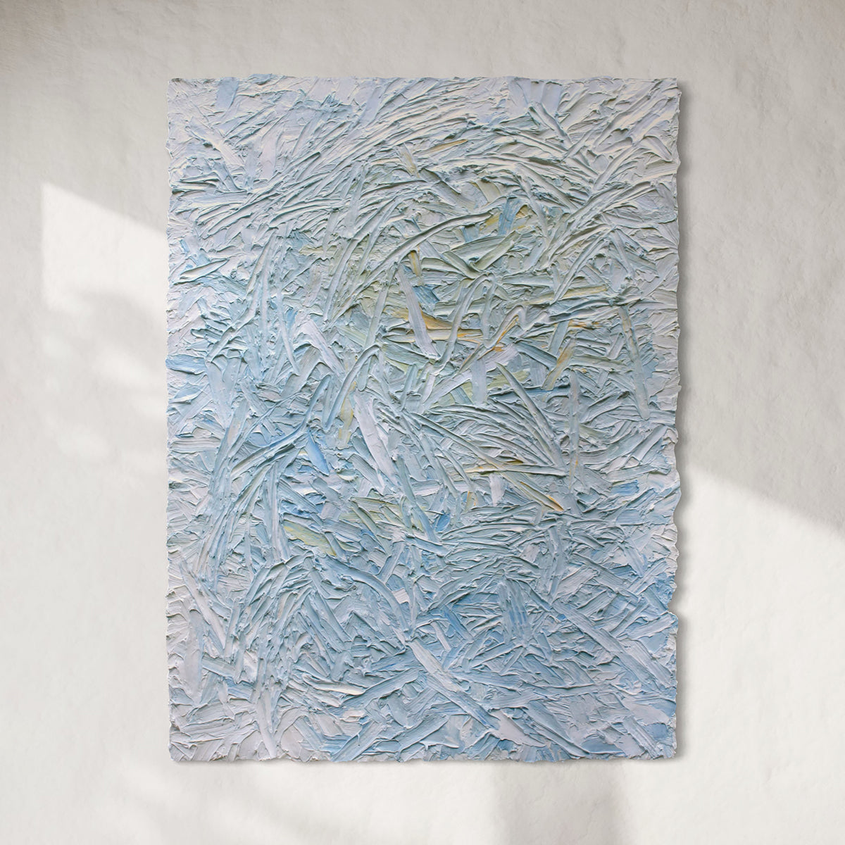 Original abstract textured painting with blue and white tones hanging on a sun light white wall.