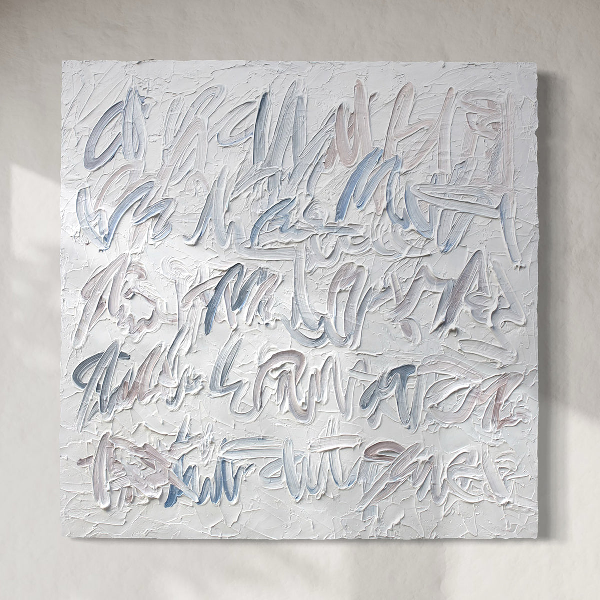An abstract text based painting featuring textured, impasto brushstrokes in shades of light blue, gray, and off-white, mounted on a neutral beige wall.