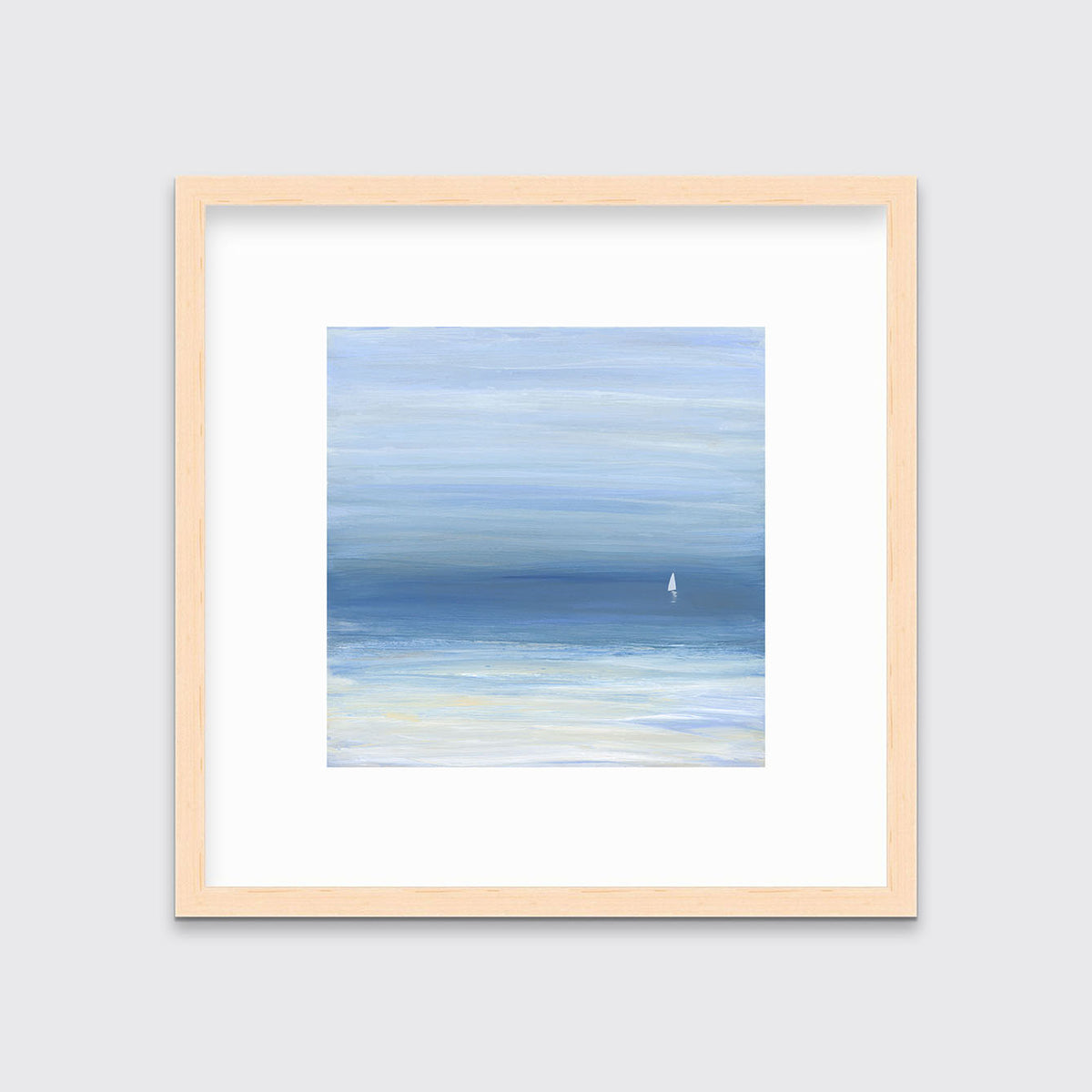 A blue, beige and white abstract seascape print with a small sailboat in a natural wood frame with a mat hangs on a white wall.
