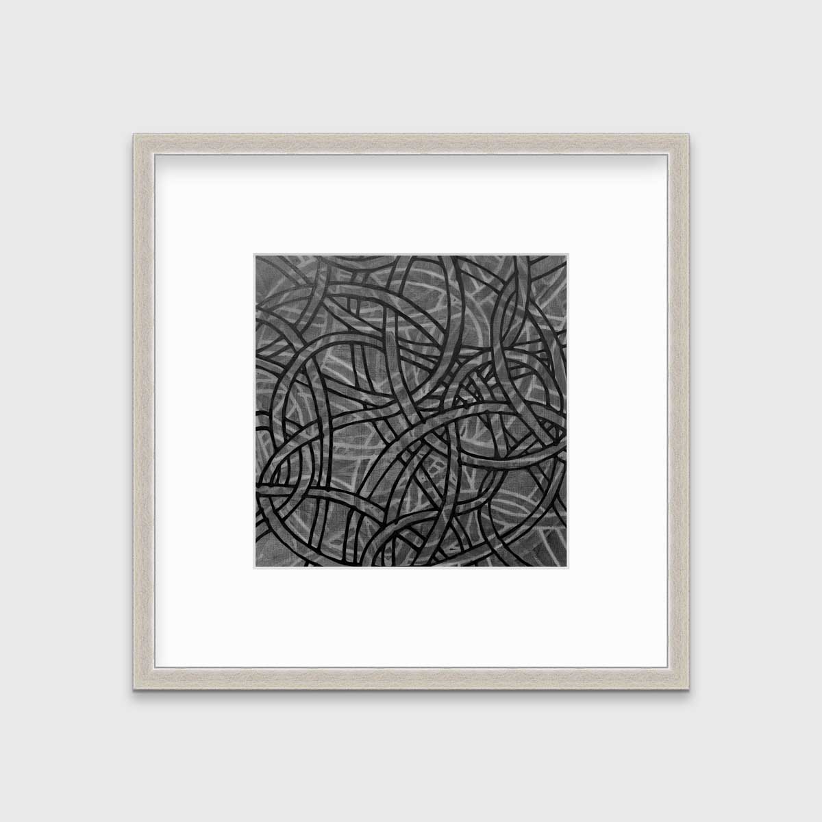 A grey, black and white abstract print in a silver frame with a mat hangs on a white wall.