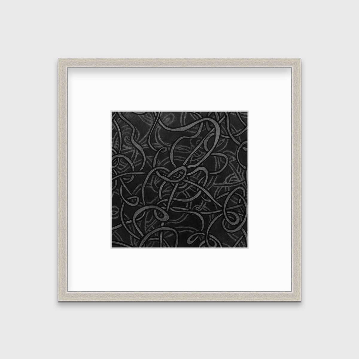 A black and grey abstract print in a silver frame with a mat hangs on a white wall.