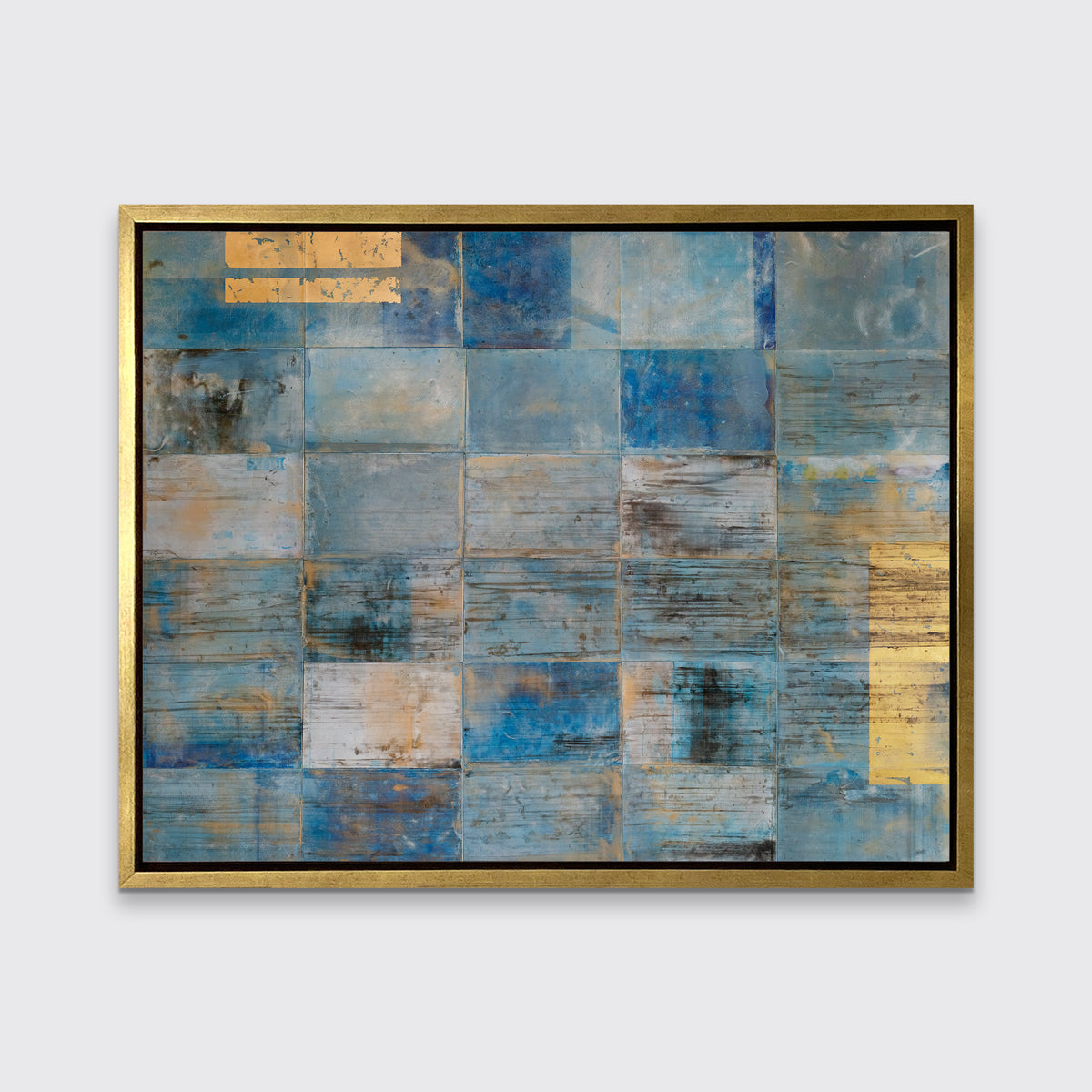 A blue and gold geometric abstract print in a gold floater frame hangs on a white wall.