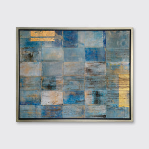 A blue and gold abstract geometric print in a silver floater frame hangs on a white wall.