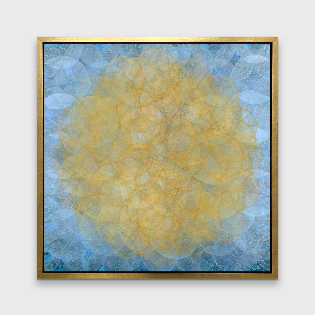 A blue, golden yellow and white abstract geometric print in a gold floater frame hangs on a white wall.
