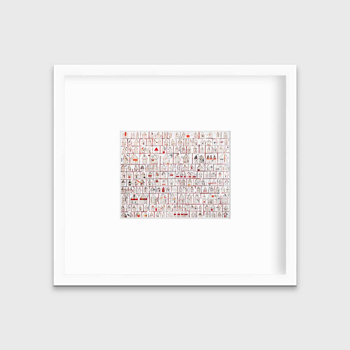 A red and white abstract house print in a white frame with a mat hangs on a white wall.