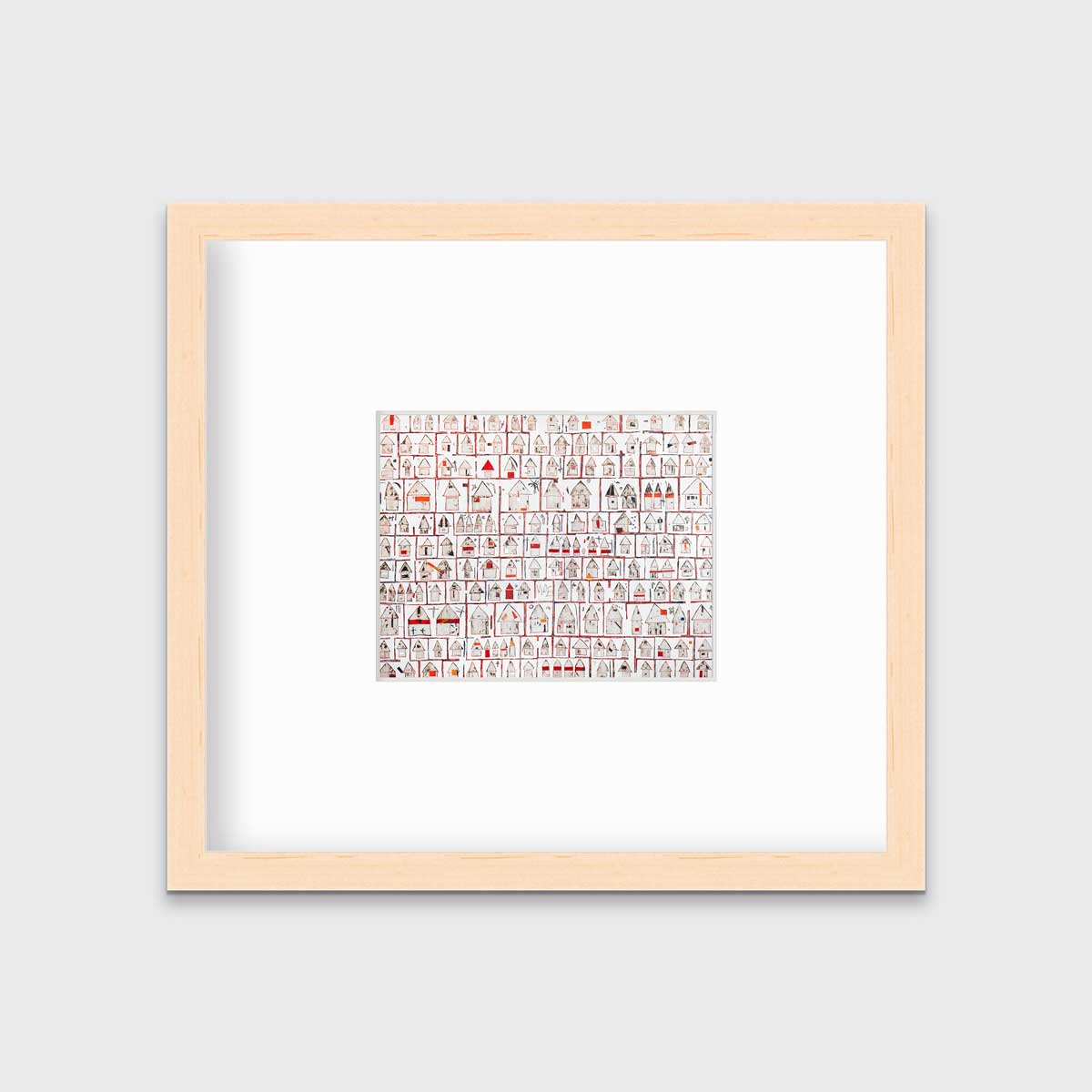 A red and white abstract house print in a natural wood frame with a mat hangs on a white wall.