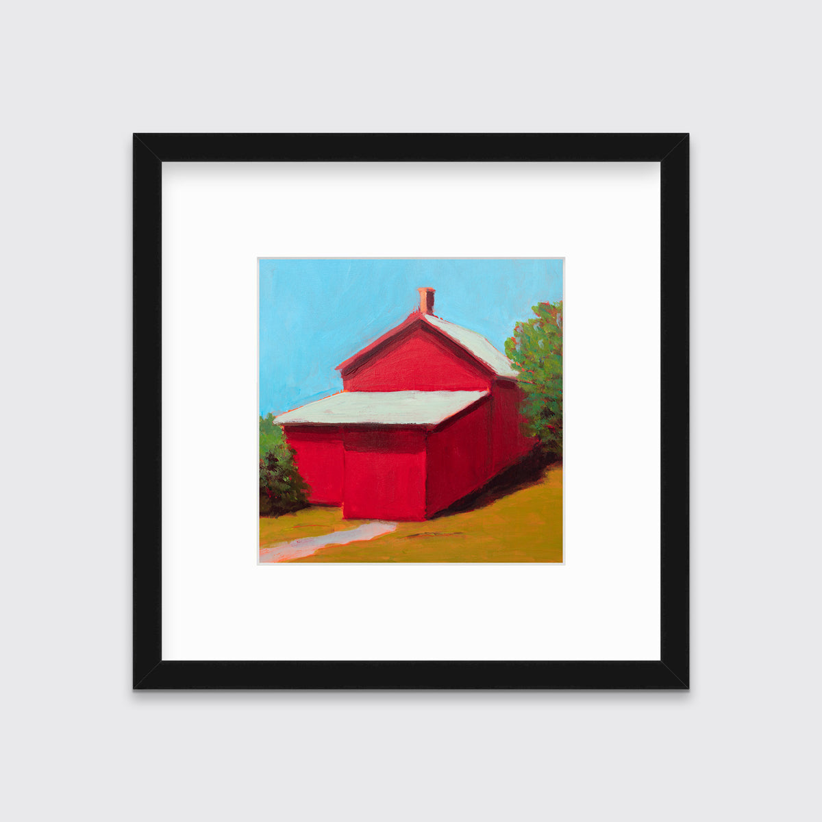 A print of a red barn with a grey roof, blue sky, green bushes and a chartreuse lawn in a black frame with a mat hangs on a white wall.