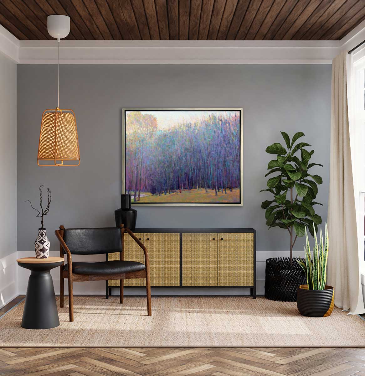 A blue and purple abstract tree landscape print in a silver floater frame hangs on a grey wall above a black and rattan low dresser with a black vase, a black chair and a side table with black and white vase. Two potted plants sit in the right corner.