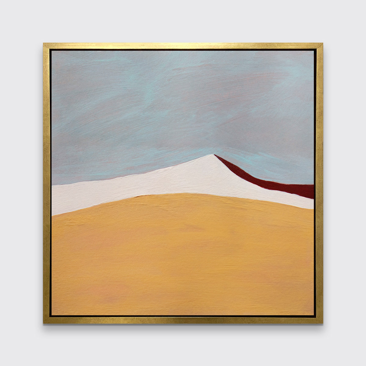 A dark yellow, white, dark red and slate blue abstract landscape print in a gold floater frame hangs on a white wall.
