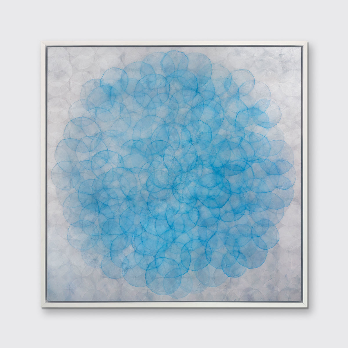 A silver and blue abstract geometric print in a white floater frame hangs on a white wall.