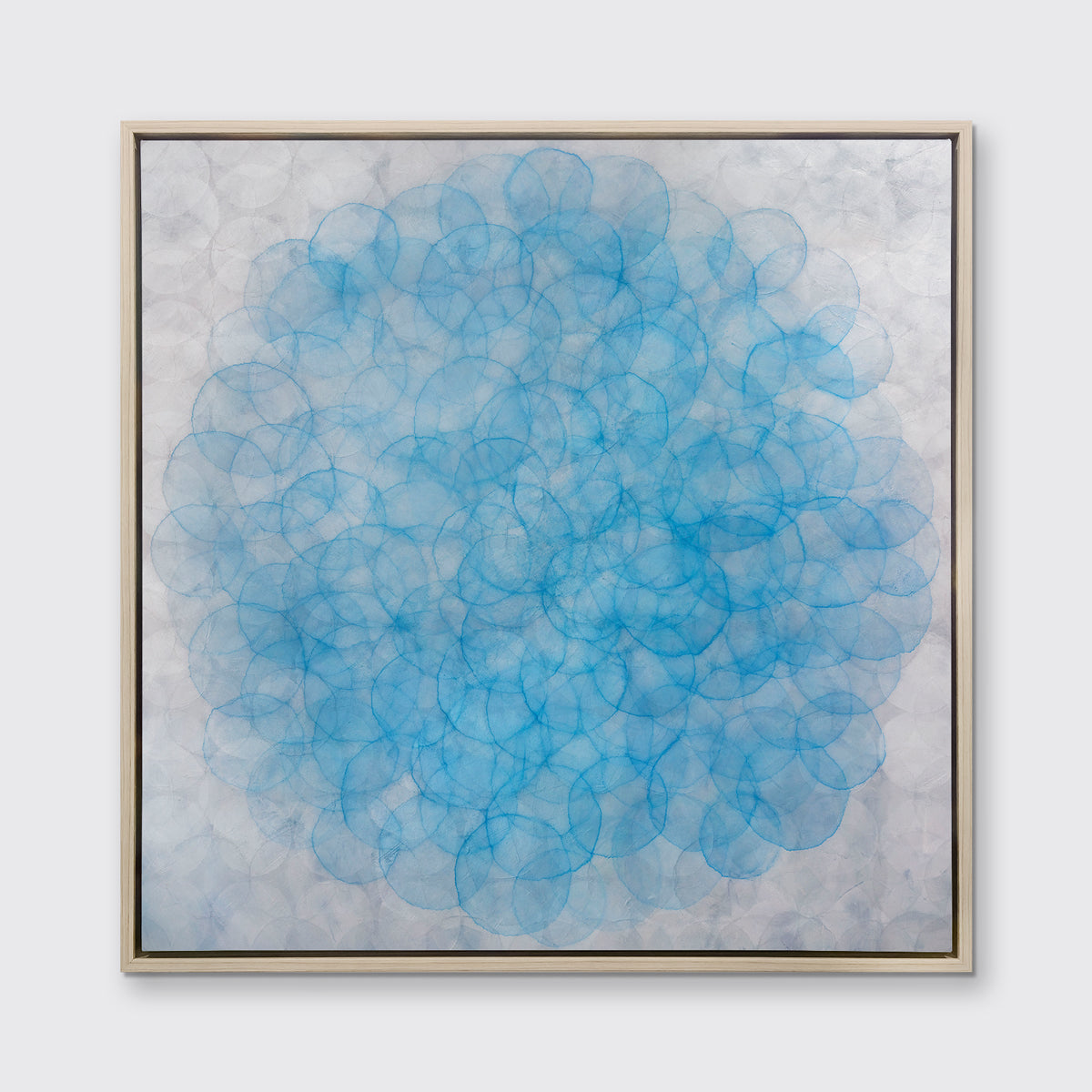 A silver and blue abstract geometric print in a white oak wood floater frame hangs on a white wall.