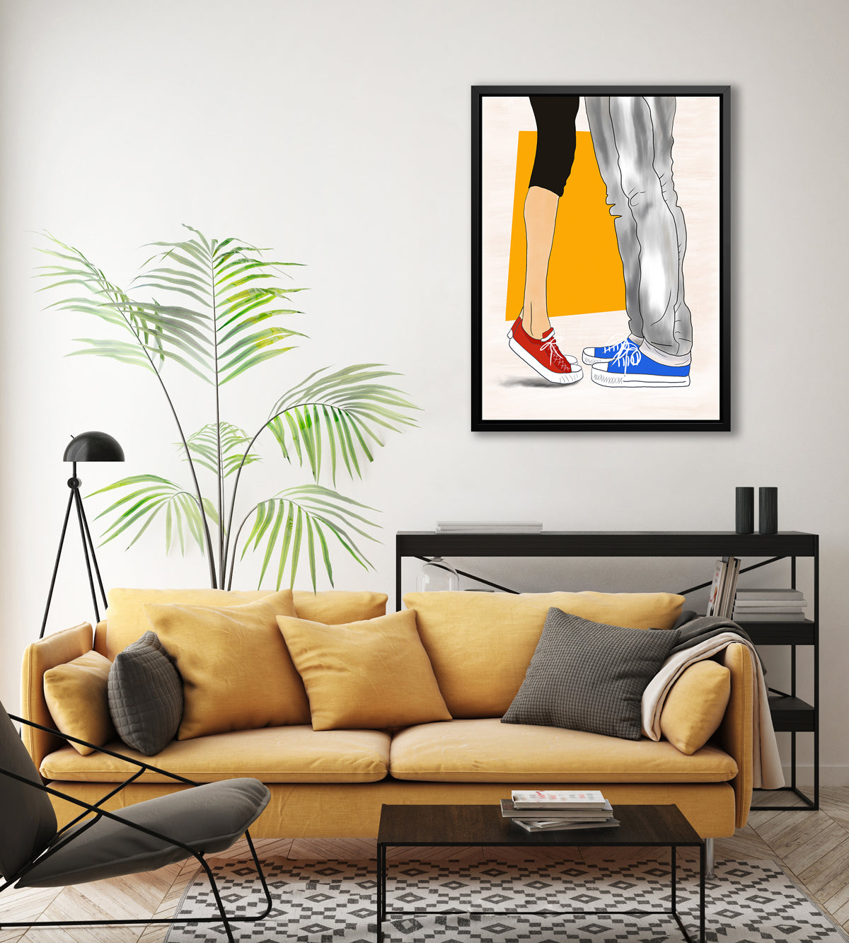 Art print with man and woman wearing Converse sneakers, framed in a black floater frame hangs on a white wall above a black bookshelf and a dark yellow sofa with pillows.