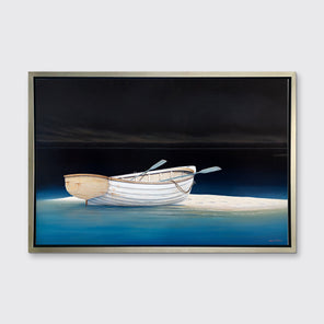 A contemporary realist print of a white rowboat alone on a sandbank in dark water against a dark sky in a silver floater frame hangs on a white wall.