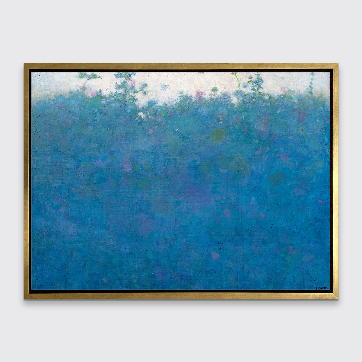 A blue, green, pink and white abstract landscape print in a gold floater frame hangs on a white wall.