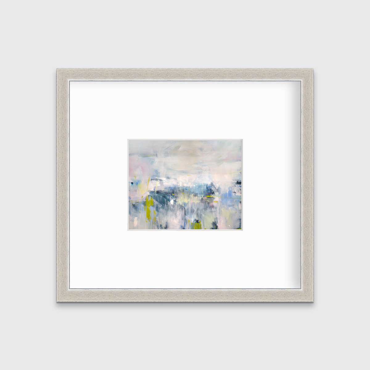 A pink and blue abstract print in a silver frame with a mat hangs on a white wall.