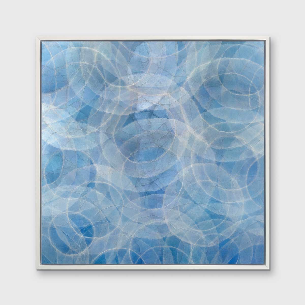 A blue and white abstract geometric print in a white floater frame hangs on a white wall.
