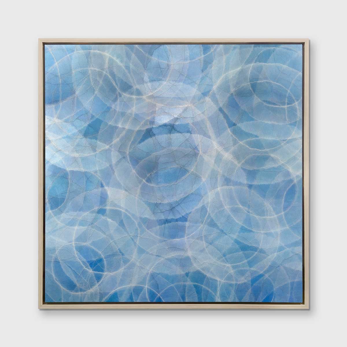 A blue and white abstract geometric print in a white oak wood floater frame hangs on a white wall.