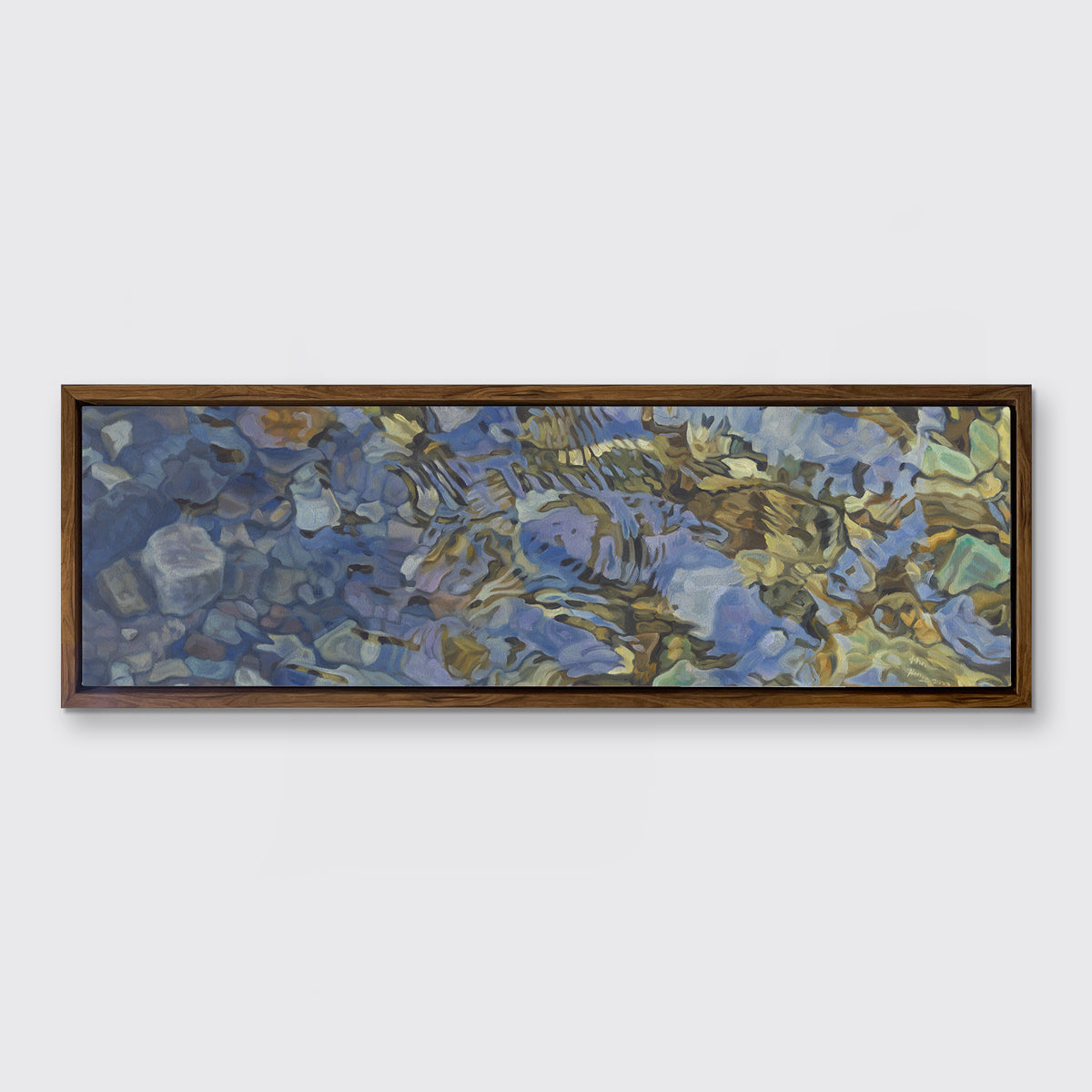 A brown, dark green, white and light blue abstract river rocks in water print in an oak wood floater frame hangs on a white wall.