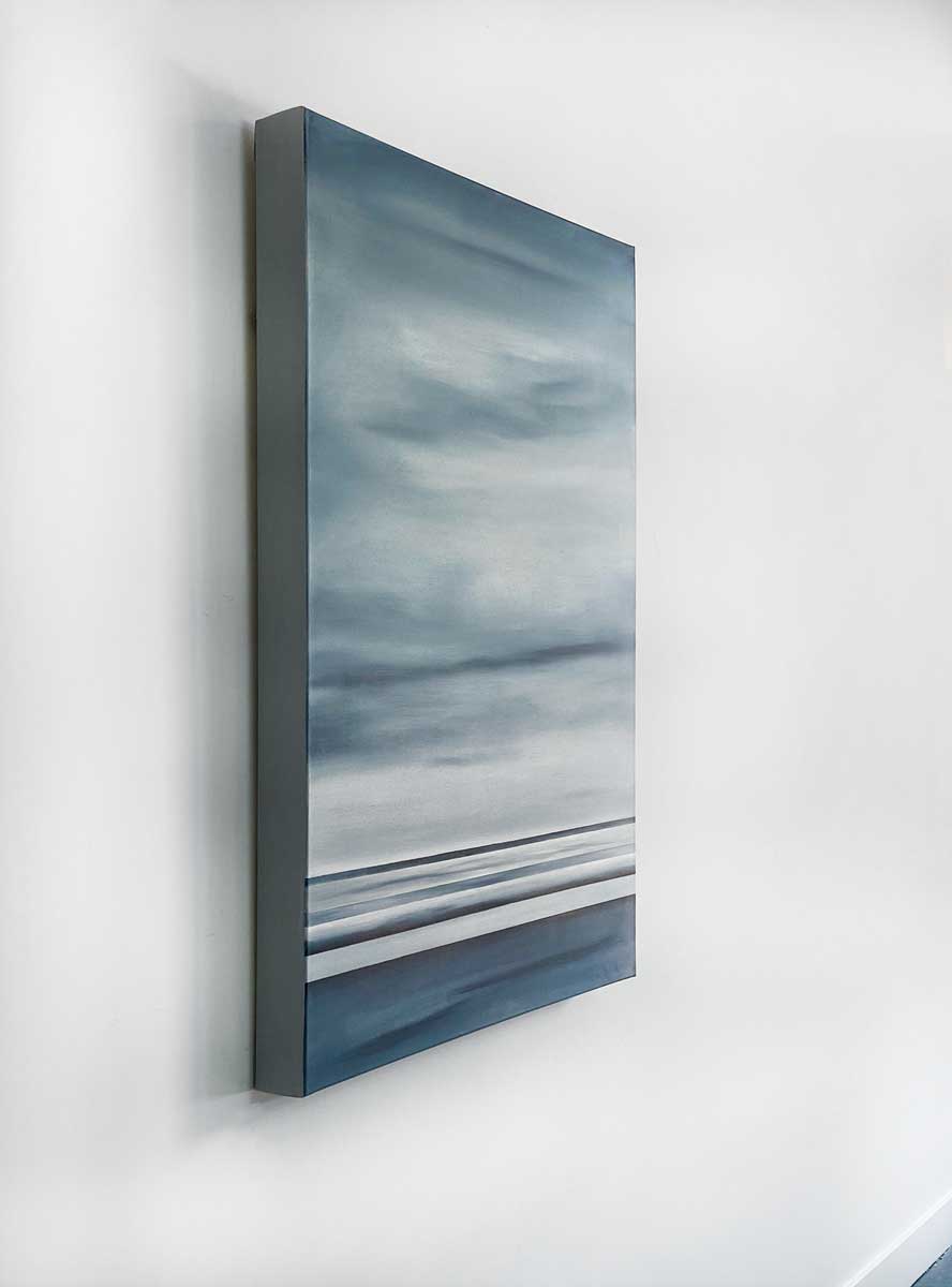 A left side-angle view of a blue and grey abstract geometric painting hanging on a white wall.