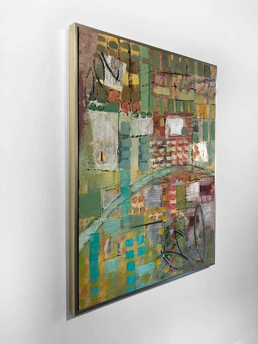 A side-angle view of an earth-toned encaustic painting, framed in a gold frame and hung on a white wall.