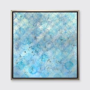 A blue and silver abstract circle print in a silver floater frame hangs on a white wall.