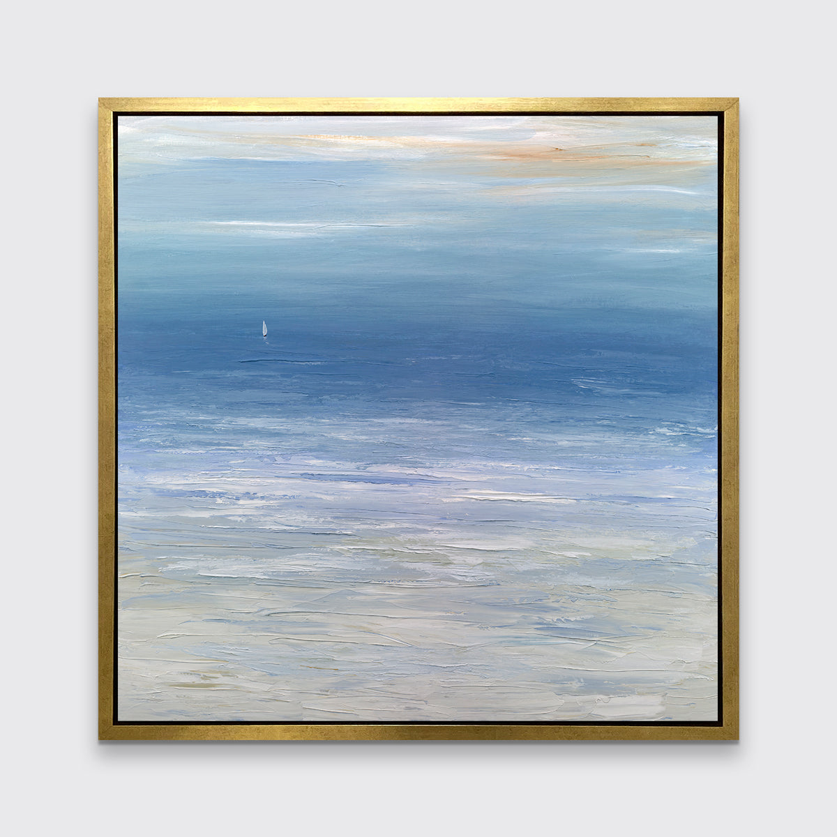 A blue, white and beige abstract seascape print in a gold floater frame hangs on a white wall.