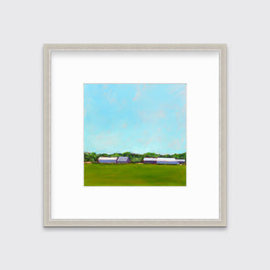 A blue, green, lavender and white landscape print in a silver frame with a mat hangs on a white wall.