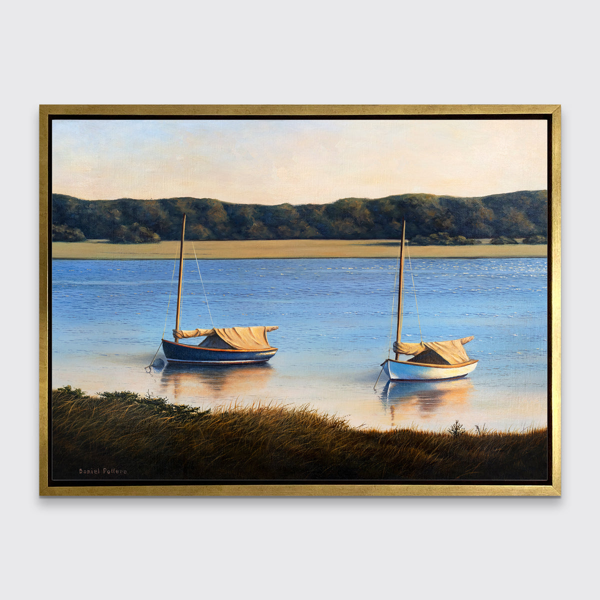 A contemporary realist print of two anchored boats wading in the water in a gold floater frame hangs on a white wall.