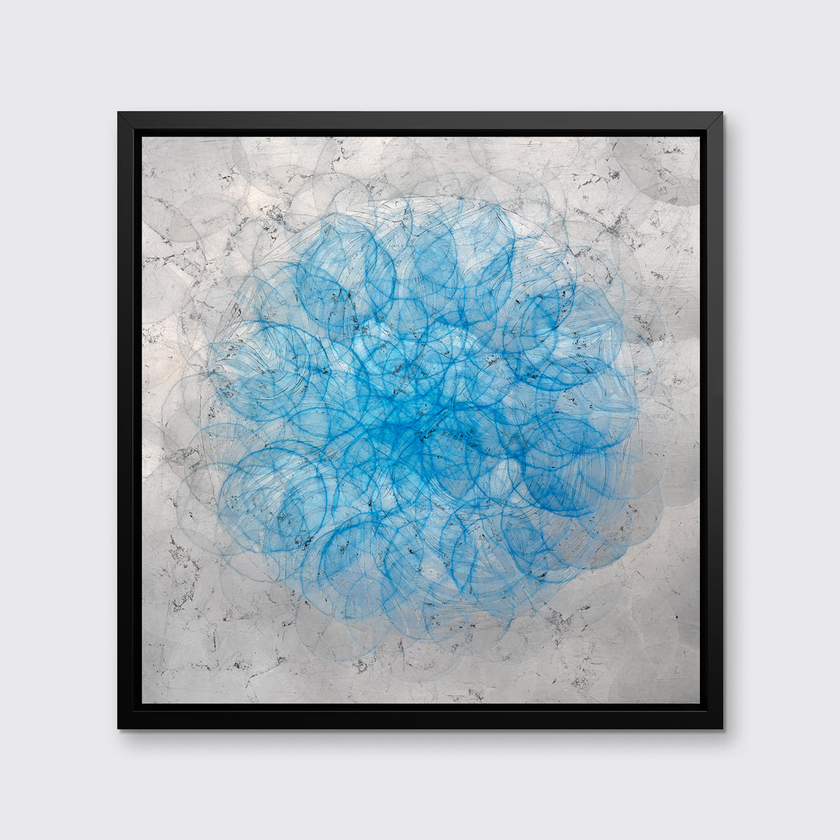 A silver, grey and blue abstract overlapping circle print in a black floater frame hangs on a white wall.