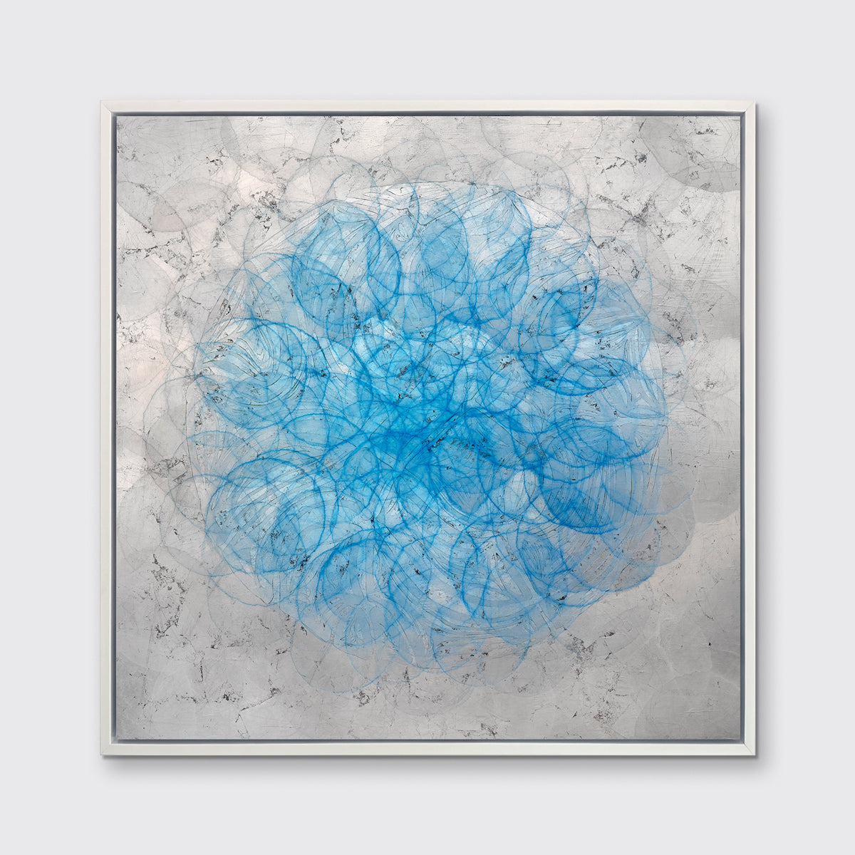 A silver, grey and blue abstract overlapping circle print in a white floater frame hangs on a white wall.