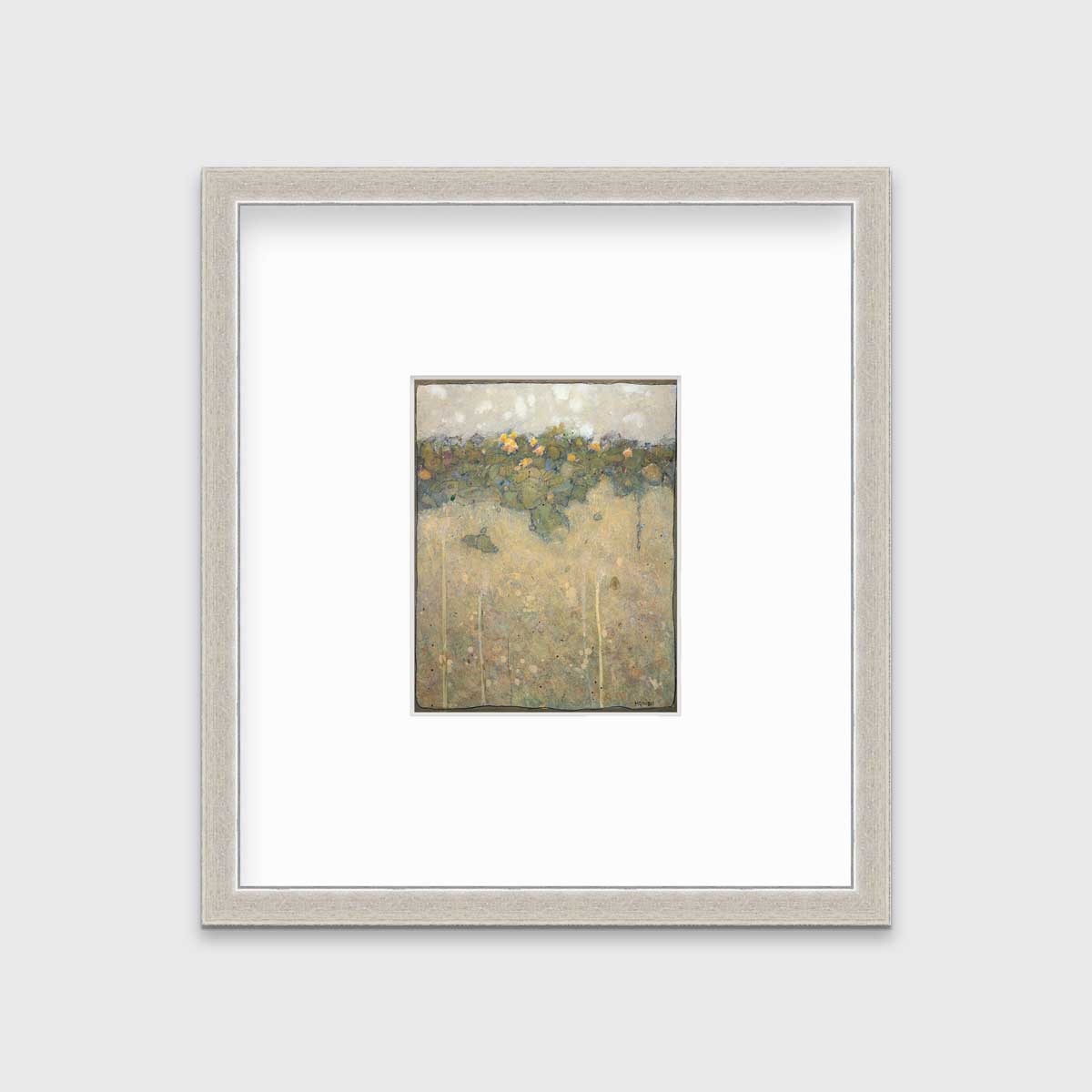 A muted yellow, green and beige abstract landscape print in a silver frame with a mat hangs on a white wall.