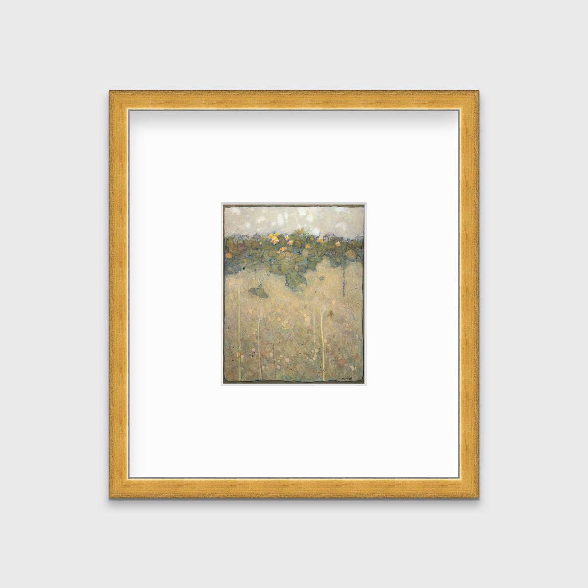 A muted yellow, green and beige abstract landscape print in a gold frame with a mat hangs on a white wall.