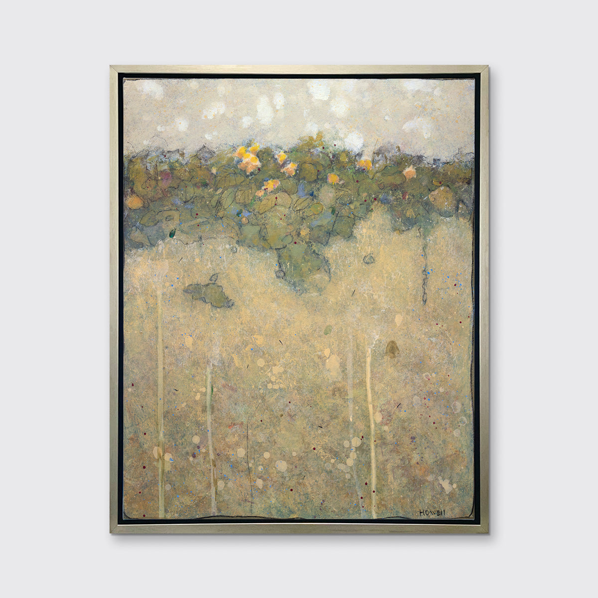 A muted yellow, green and beige abstract landscape print in a silver floater frame hangs on a white wall.