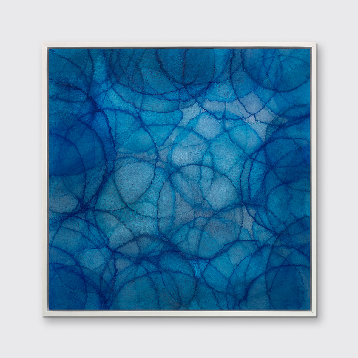 A blue and light blue abstract overlapping circle print in a white floater frame hangs on a white wall.