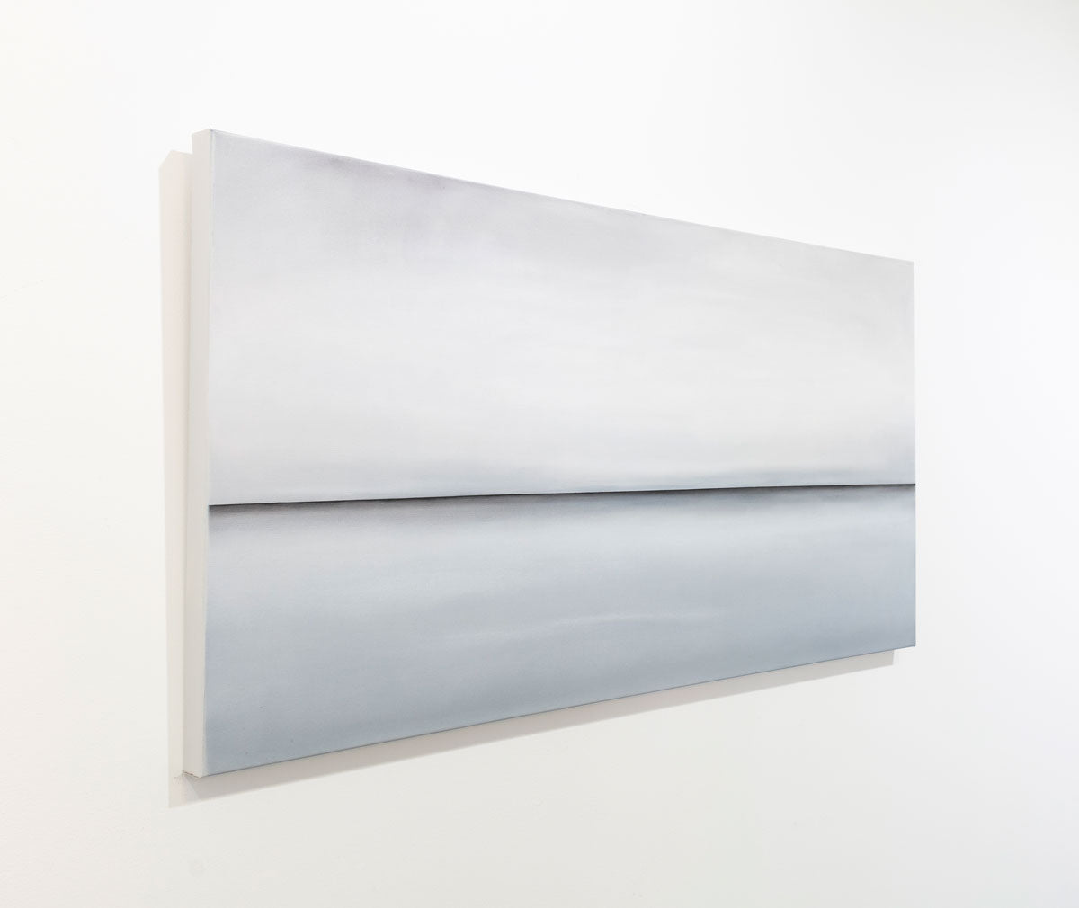 A long grey oil painting with a single black line in the middle of the canvas which suggests a horizon line is seen at an angle on a gallery wall. Wired and ready to hang.