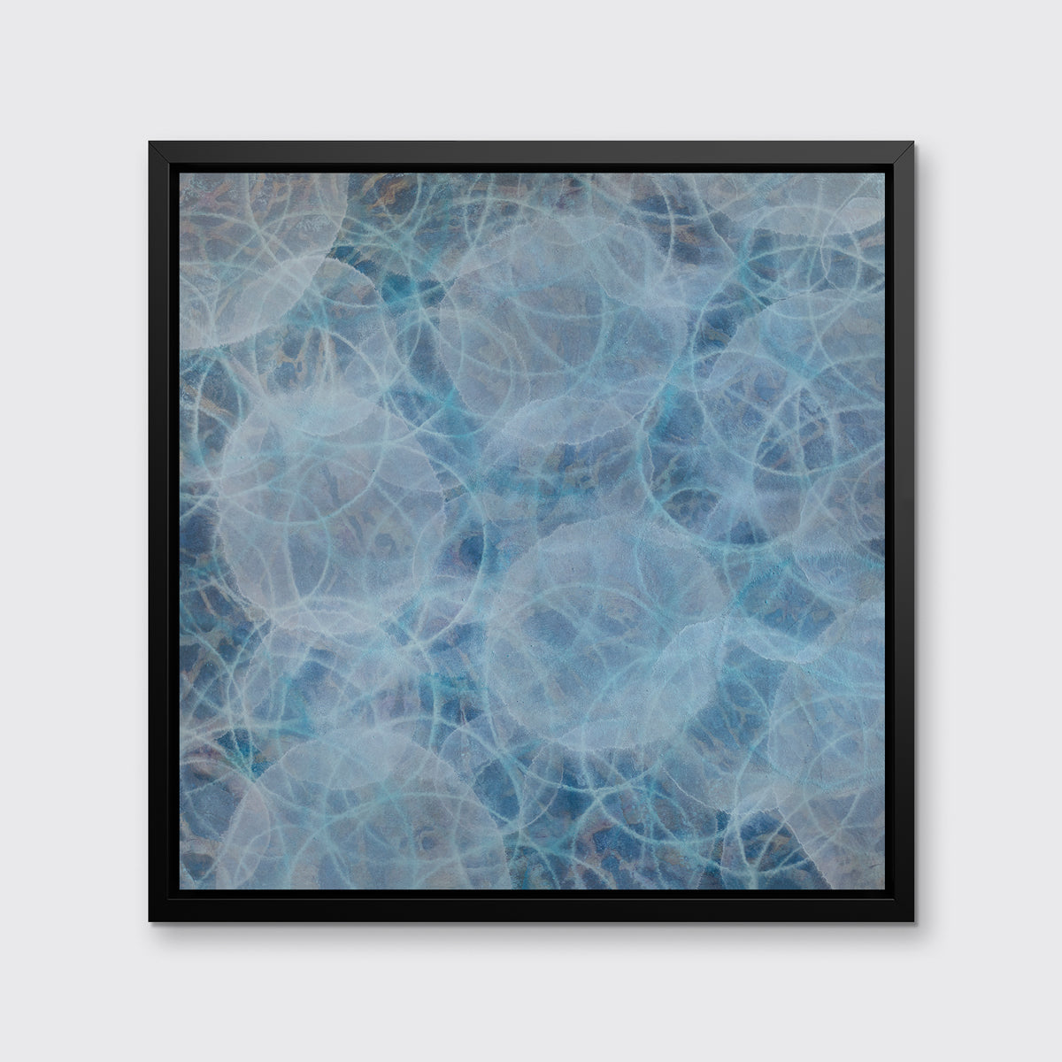A blue and teal abstract overlapping circle print in a black floater frame hangs on a white wall.