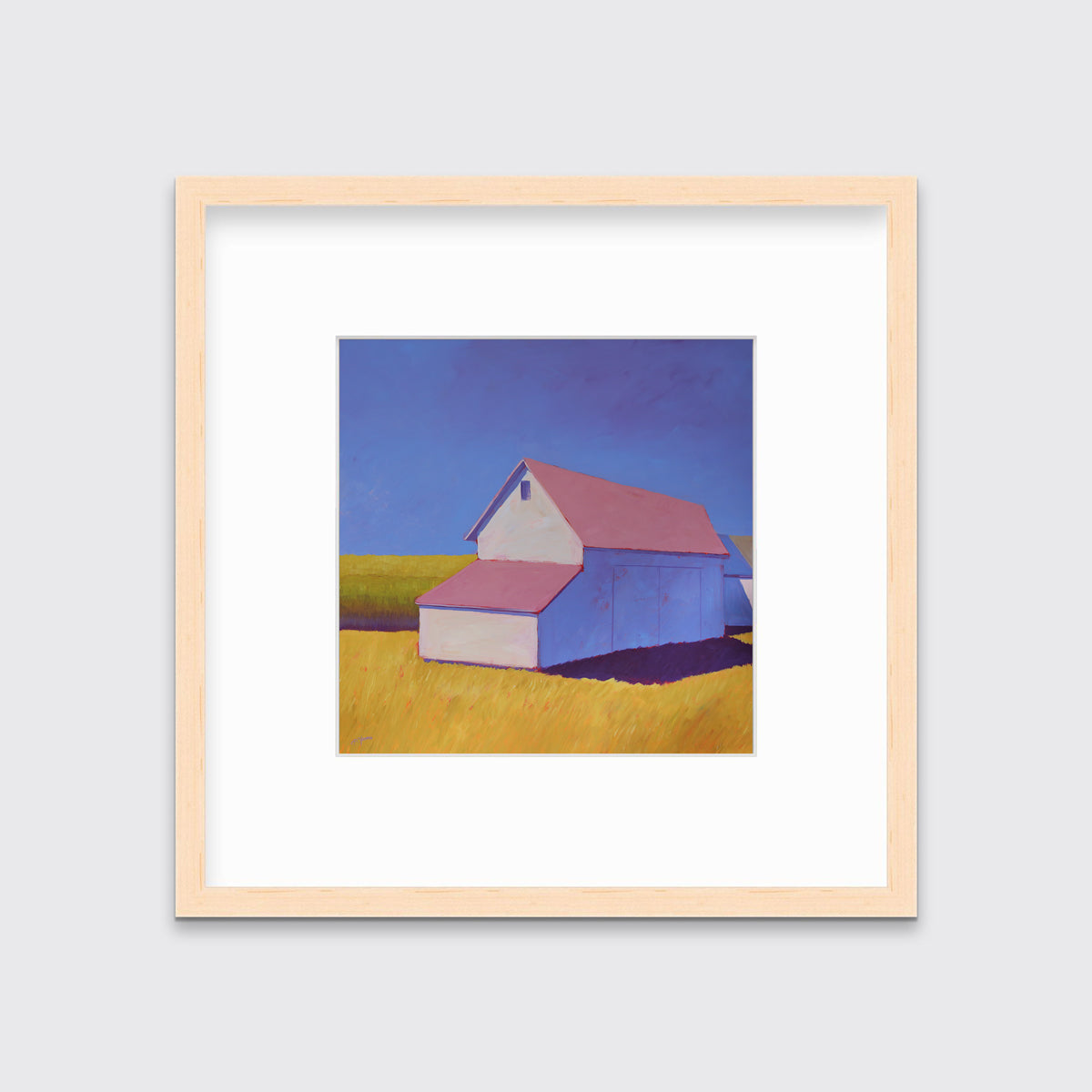 A white barn with a pink roof and yellow grass print in a natural wood frame with a mat hangs on a white wall.