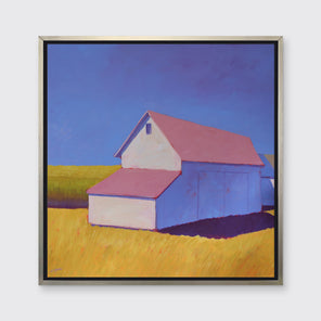 A white barn with a pink roof and yellow grass print in a silver floater frame hangs on a white wall.