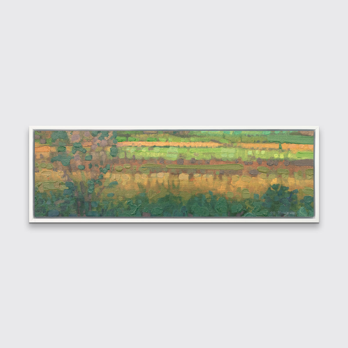 A green, yellow and deep orange abstract landscape print in a white floater frame hangs on a white wall.