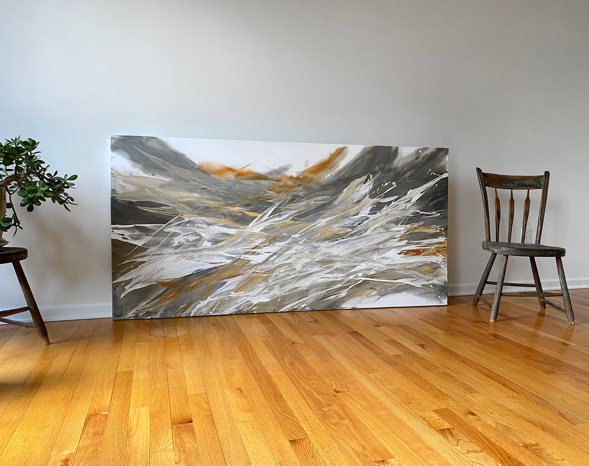 An orange, white, and black abstract painting by Teodora Guererra sits on a hardwood floor with a chair.