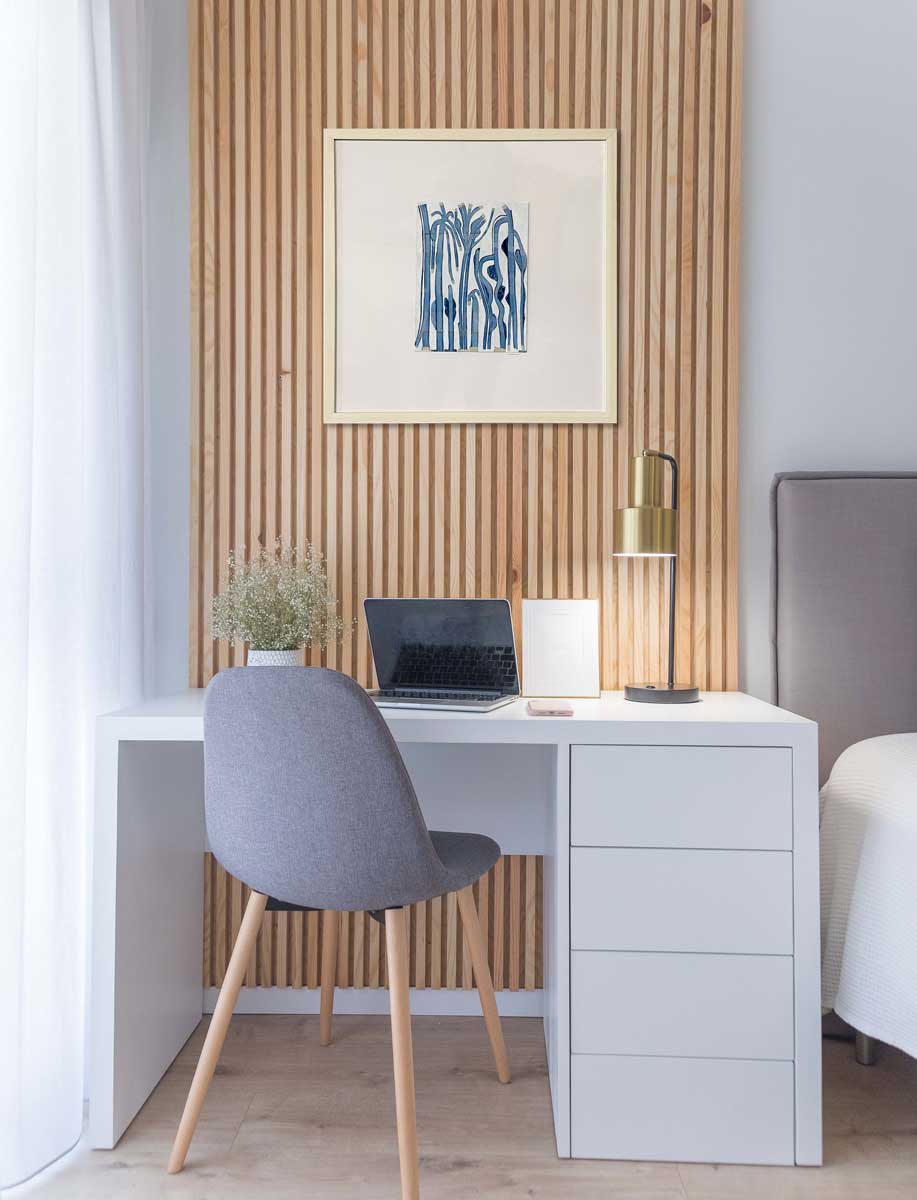 An abstract painting of blue and beige tree-like forms is hung above a desk.