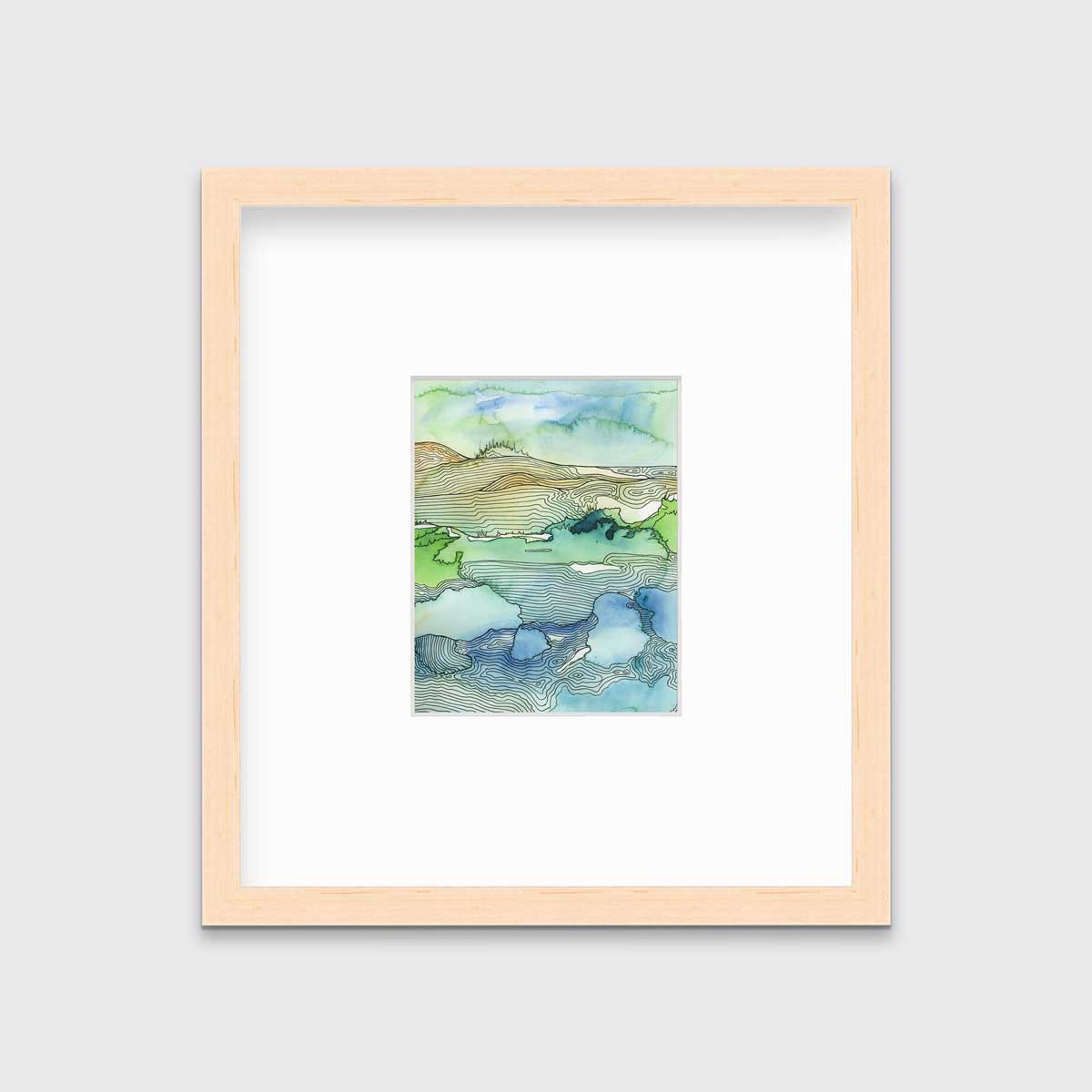 A green and blue landscape illustration print framed in a natural wood frame with a mat hangs on a light grey wall.